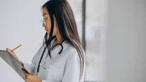 Médica com estetoscópio anotando informações em prancheta durante perícia médica.
